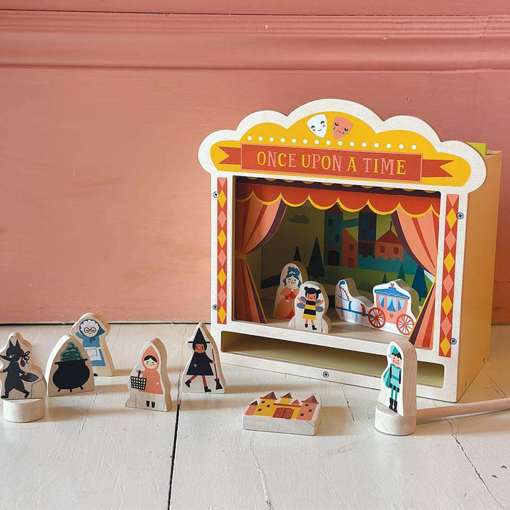 Wooden puppet theater with puppets on a light pink background