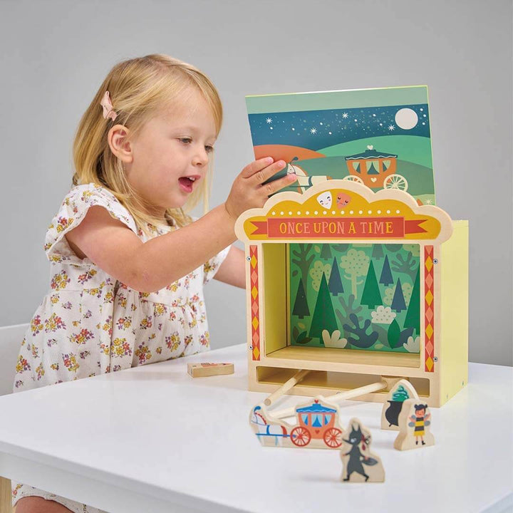 Child playing with a wooden fairy tale box toy on a white table.