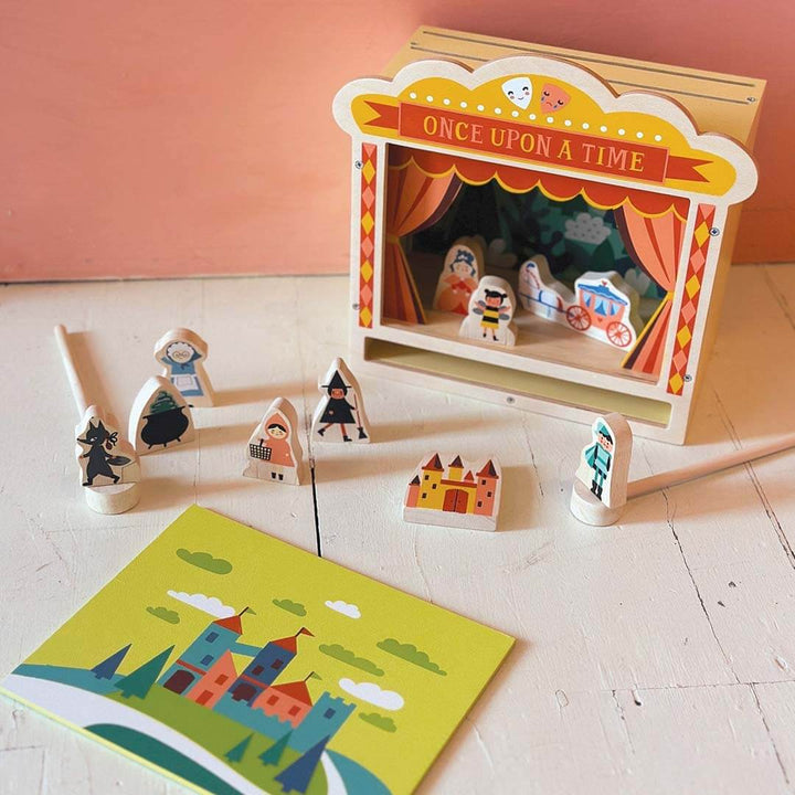 Wooden puppet theater set with puppets and a storybook on a wooden floor.