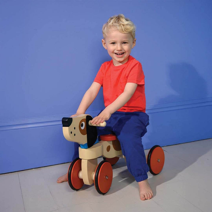 Child riding a wooden toy horse against a blue wall