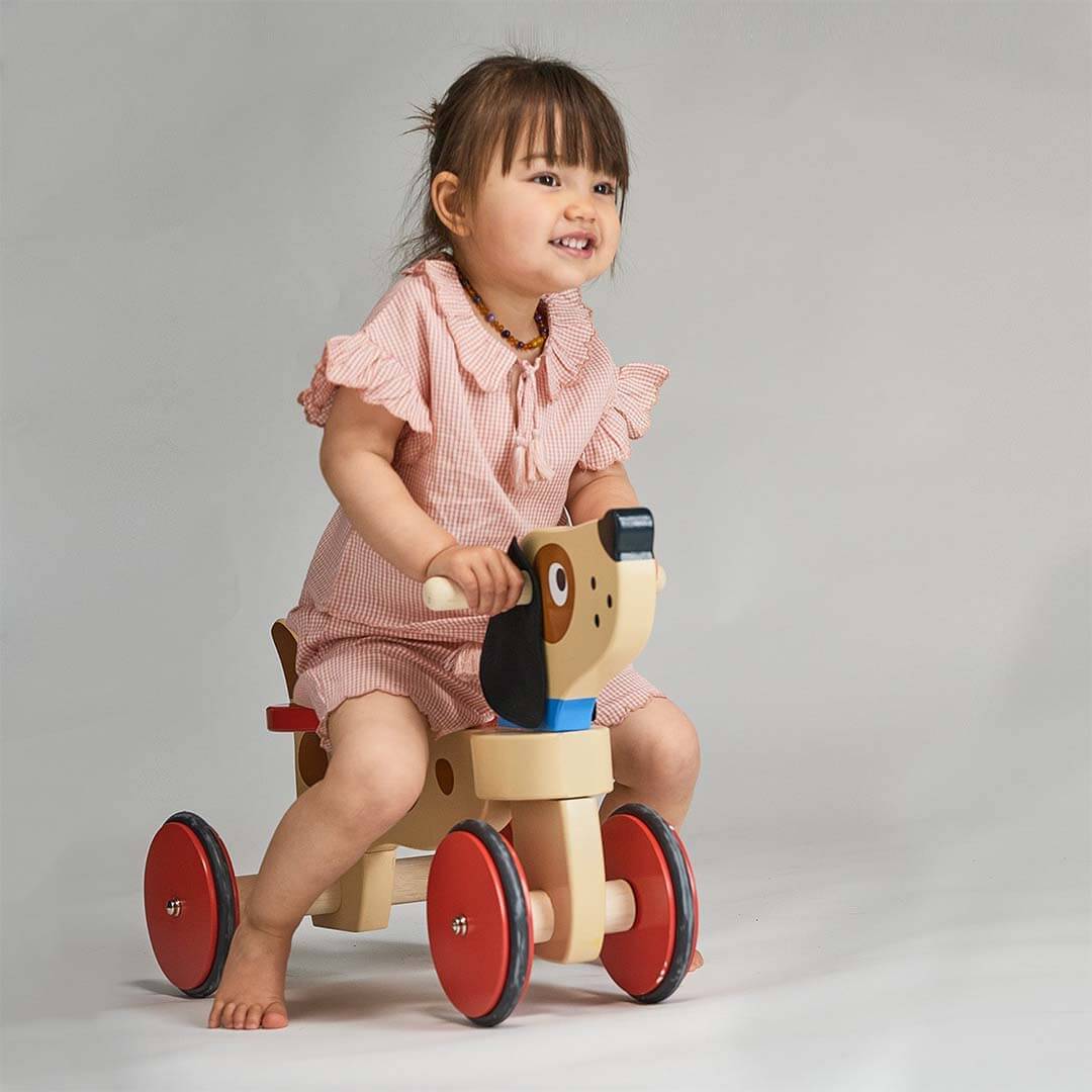Child playing with a wooden toy bike on a plain background