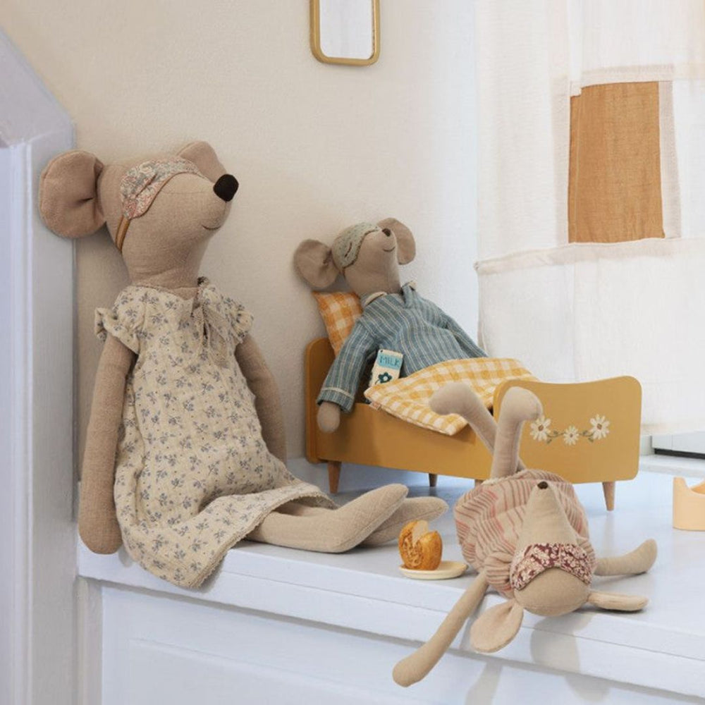 A medium Maileg mouse stuffed animals laying in a yellow doll bed next to two other stuffed mice.