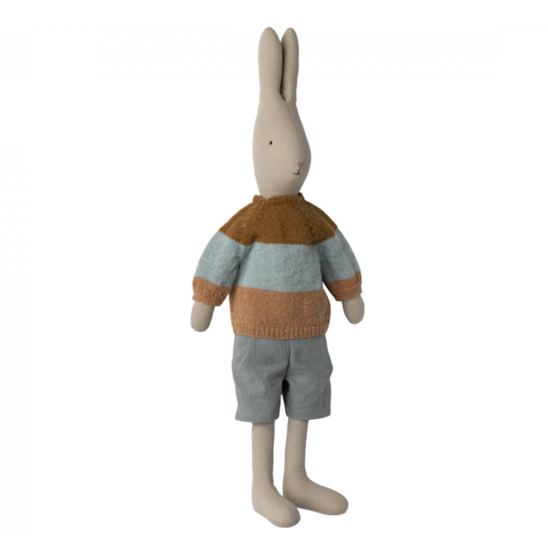 A white Maileg stuffed animal rabbit wearing a brown and blue striped sweater and grey shorts.