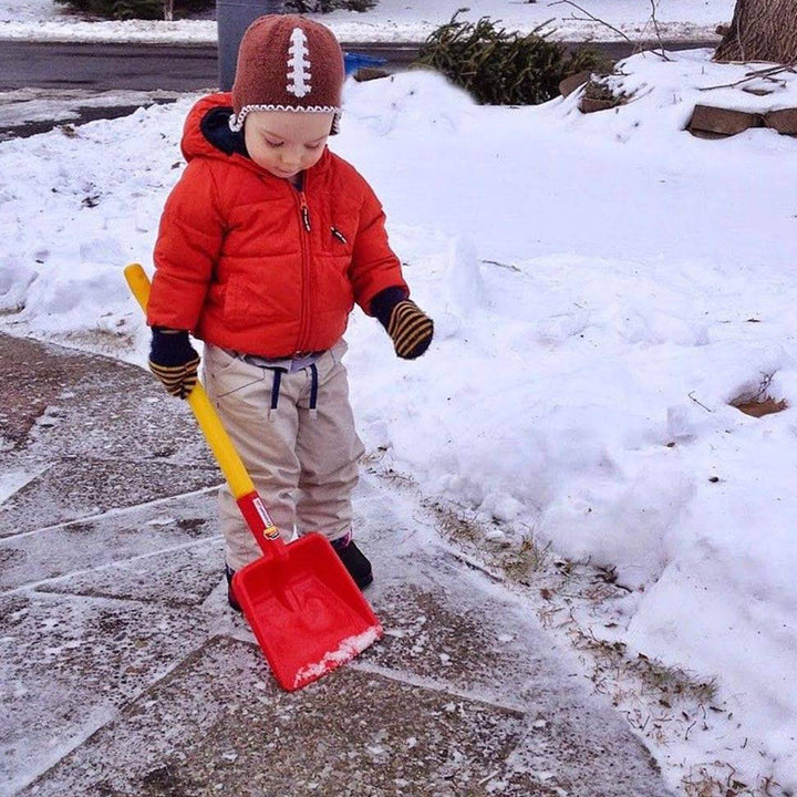Child standing in winter clothes holding a Spielstabil Long Handled Flat Shovel with snow on the ground