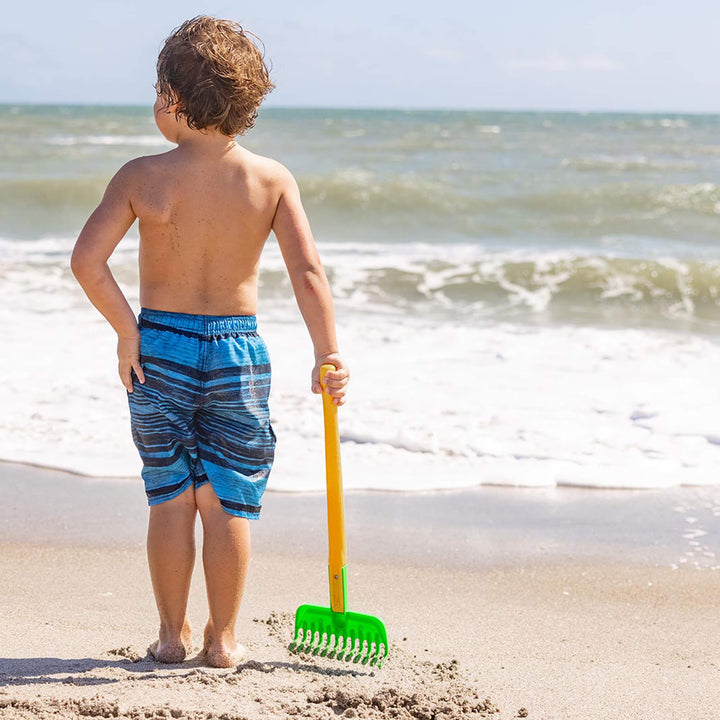 Child standing with Spielstabil Long Handled Garden Rake with ocean in the background