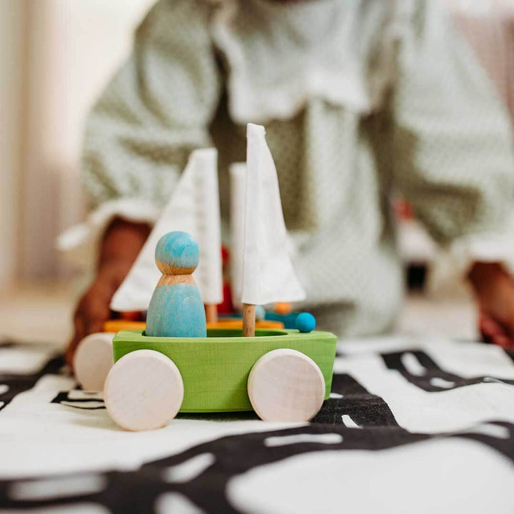 Wooden toy sailboat set on a green base with blurred person in background