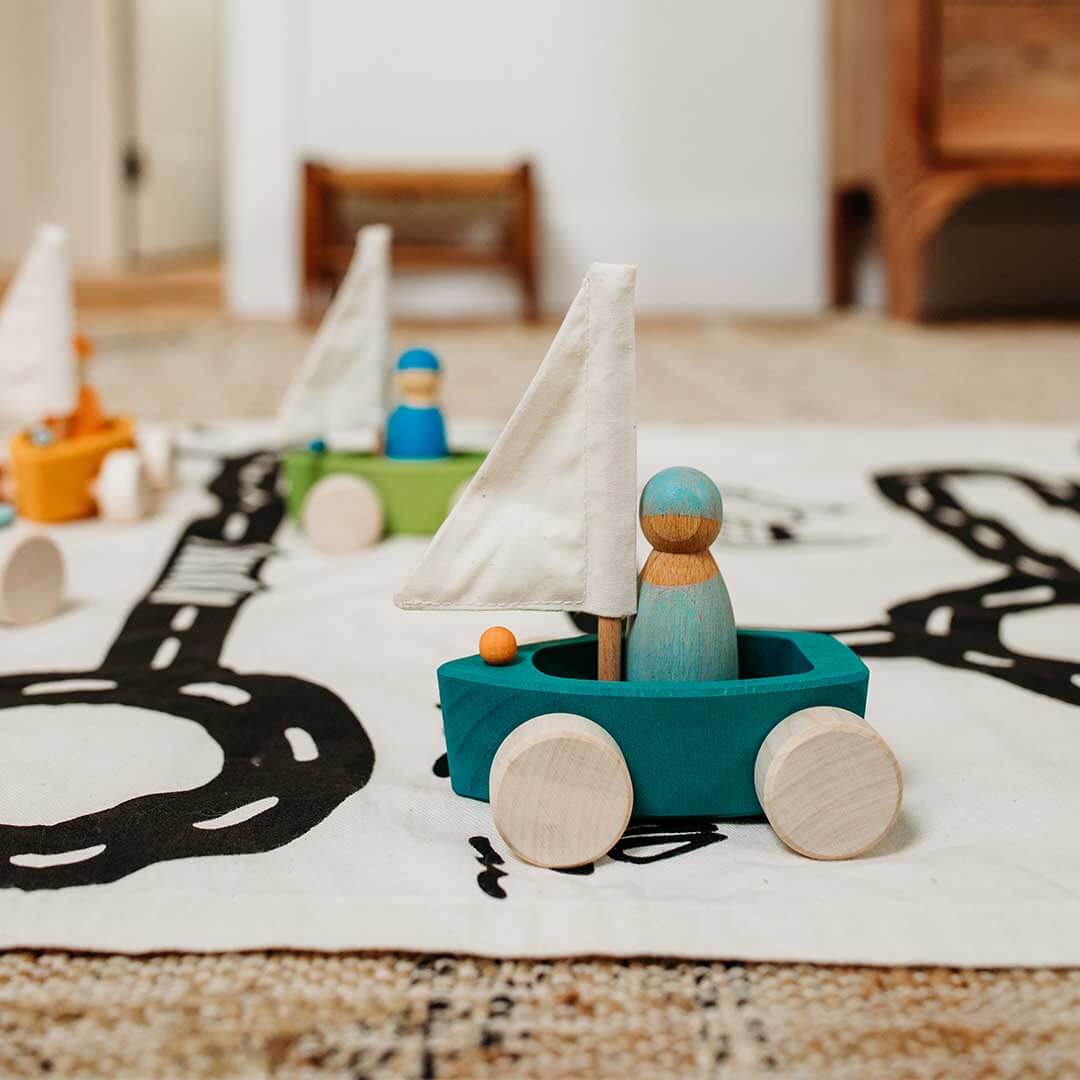 Wooden toy sailboat on a rug with other toys in the background