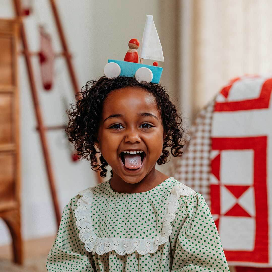 Child wearing a sailboat with a blurred indoor background