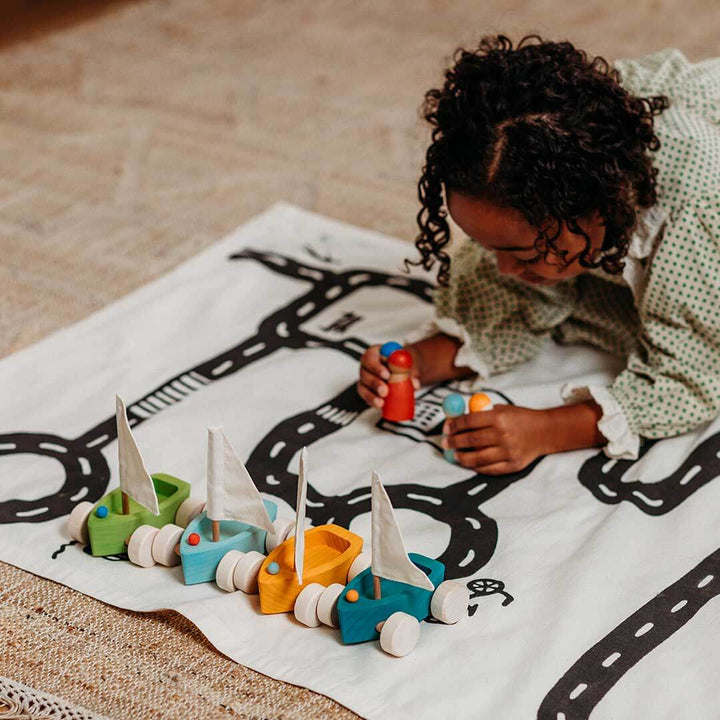 Child playing with toy boats on a blanket with road prints