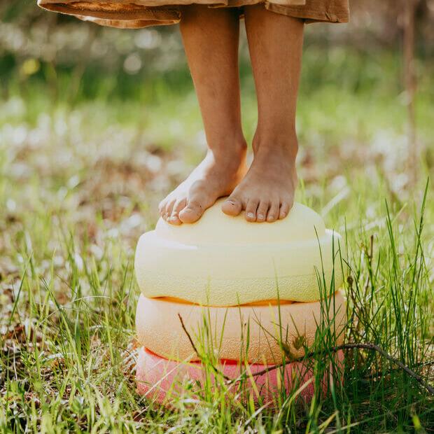 A child standing on the Stapelstein® Kids Stepping Stones Pastel Warm Colors Set.