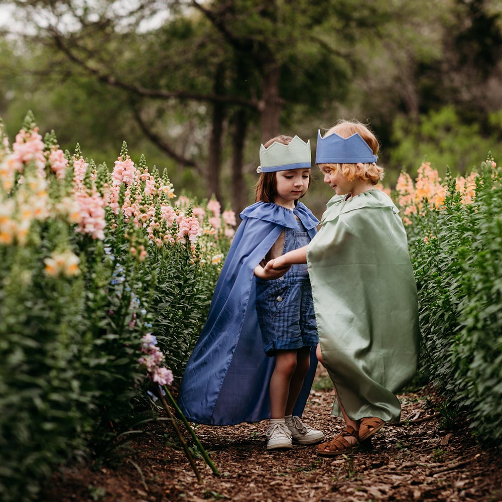 Sarah's Silks Northern Coast Magical Silk Dress Up set with reversible crowns, cape and streamer being used by two kids in a purple flower field.