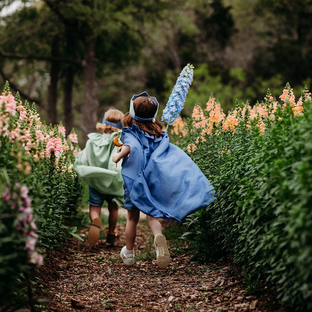 Child wearing Sarah's Silks Northern Coast Playsilk crown and cape in a flower field.