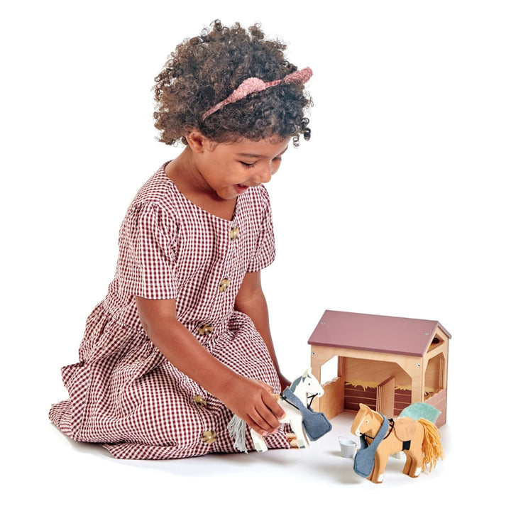 A young girl plays with a wooden horse and stable set by Tender Leaf Toys.