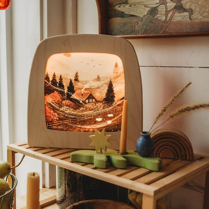 Wooden Toverlux lamp with a scenic display on a wooden shelf.