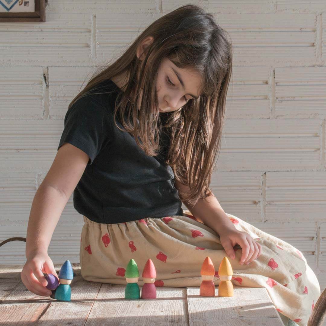 Young girl playing with colorful wooden blocks on a wooden floor.
