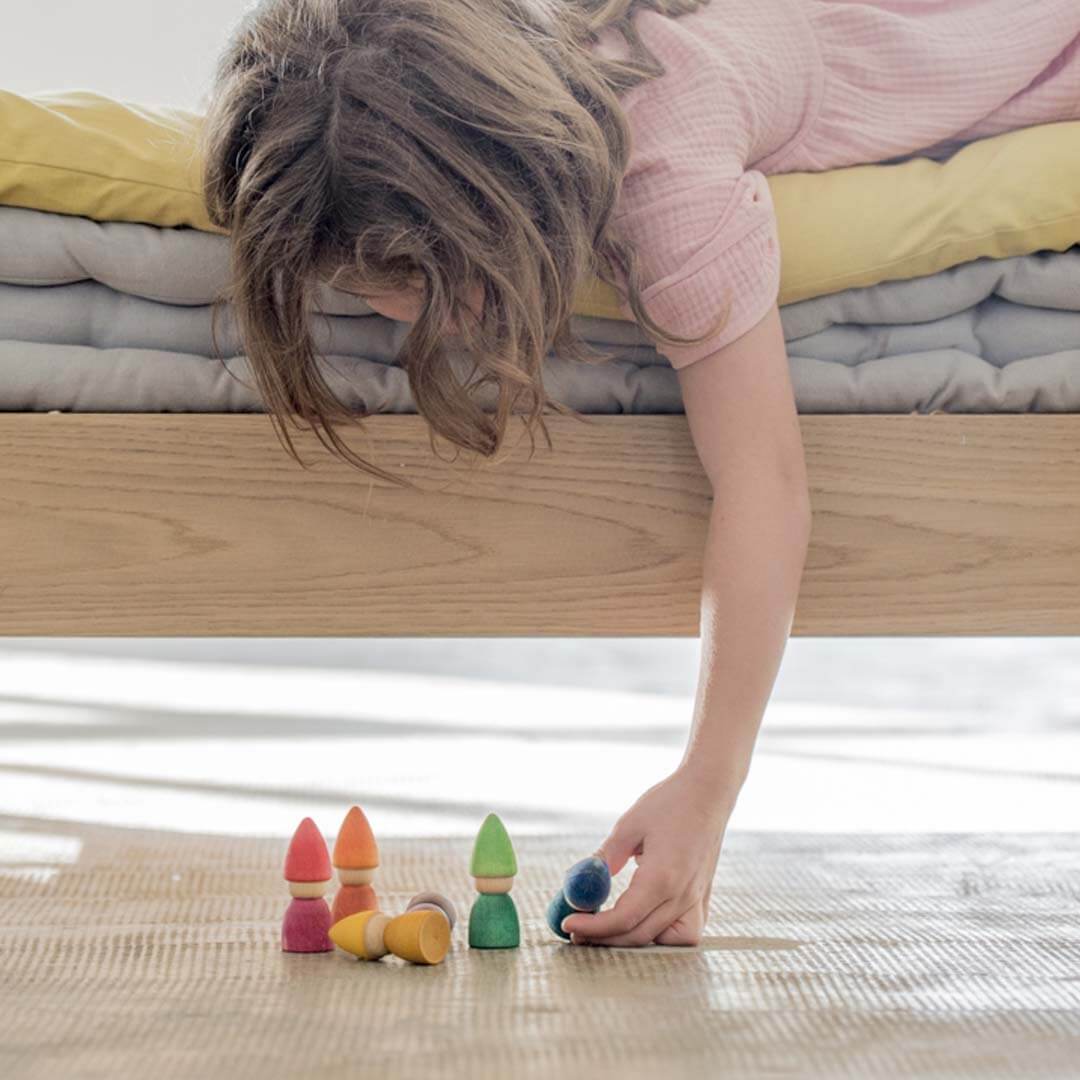 Child playing with colorful wooden toys on a bed.