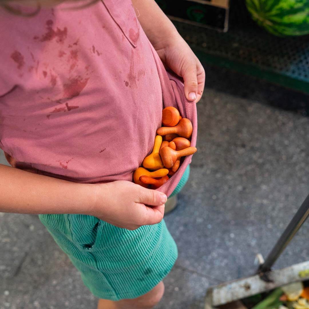 Child holding small pumpkins with a pink shirt and green shorts outdoors.