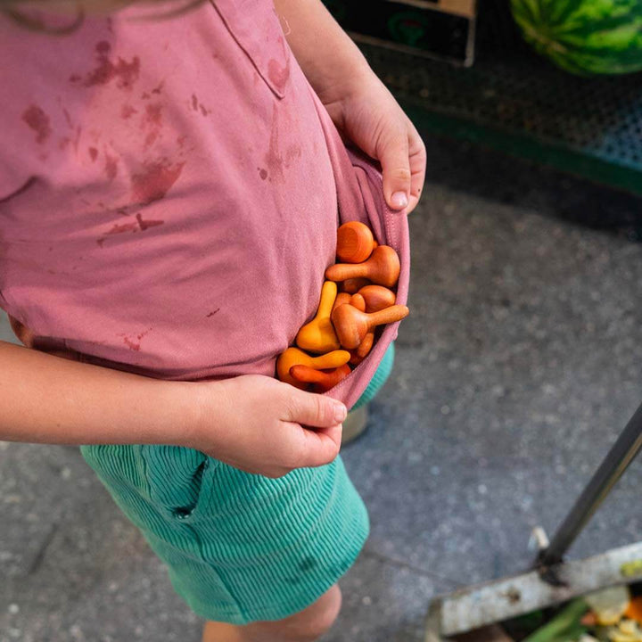 Child holding small pumpkins with a pink shirt and green shorts outdoors.