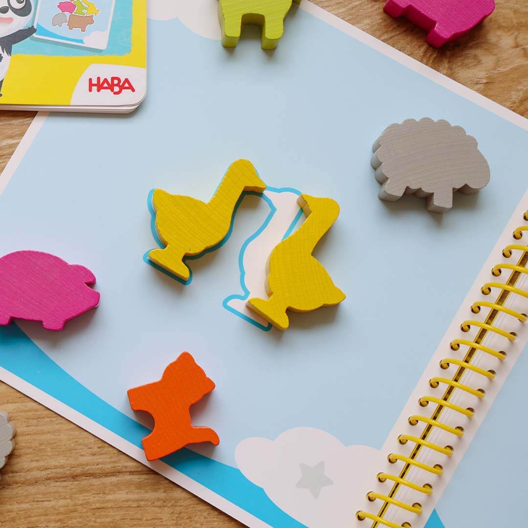 Colorful wooden animal puzzle game on a HABA card with a wooden surface underneath.