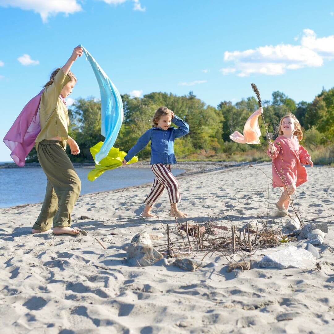 Three girls wearing and waving Bella Luna Play Silks on the beach.