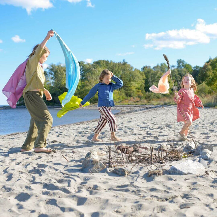 Three girls wearing and waving Bella Luna Play Silks on the beach.