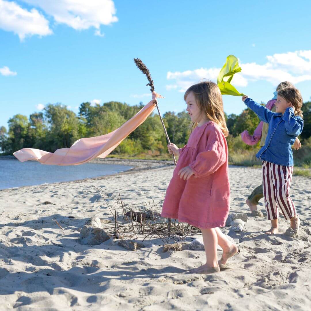 Three girls wearing and waving Bella Luna Play Silks on the beach.