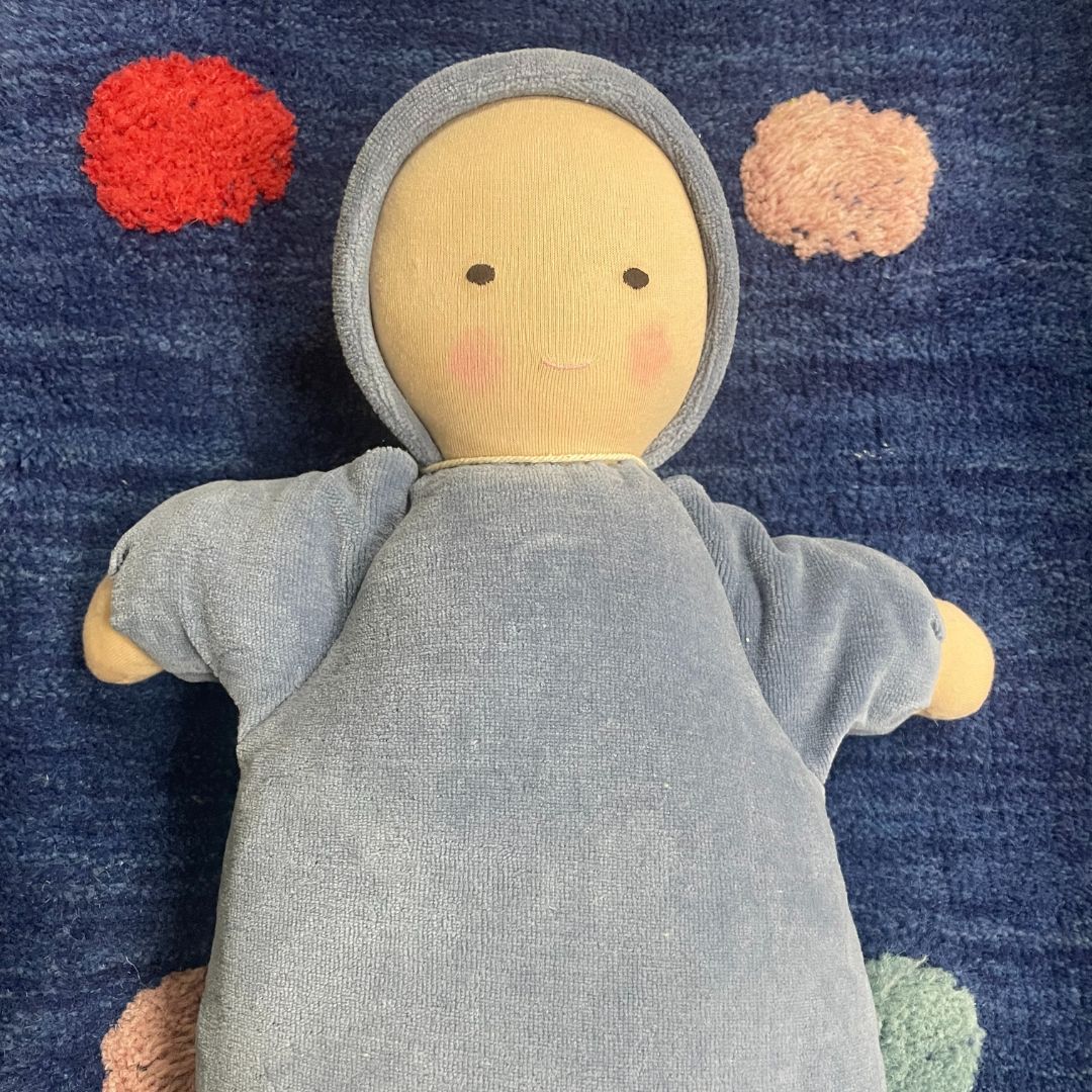 Waldorf baby doll with a light blue hood and body on a blue textured background