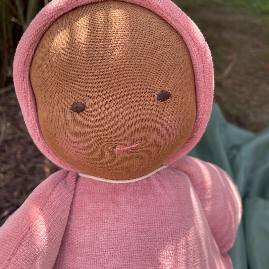 Textile doll with a brown face and pink clothing against a natural background