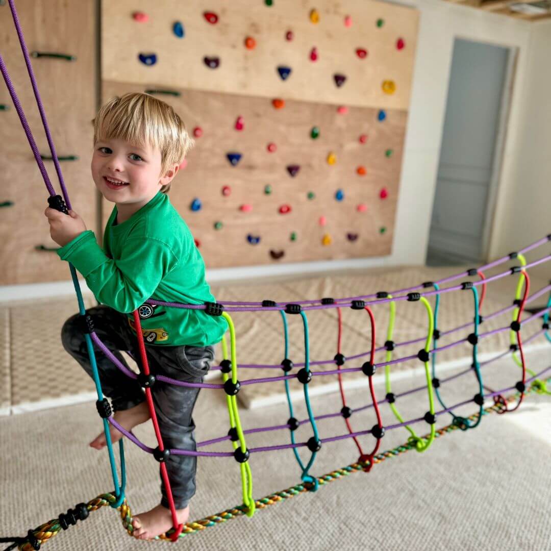A child climbing and balancing on the Bijou Rambler Rope Bridge in an indoor movement area - Bella Luna Toys