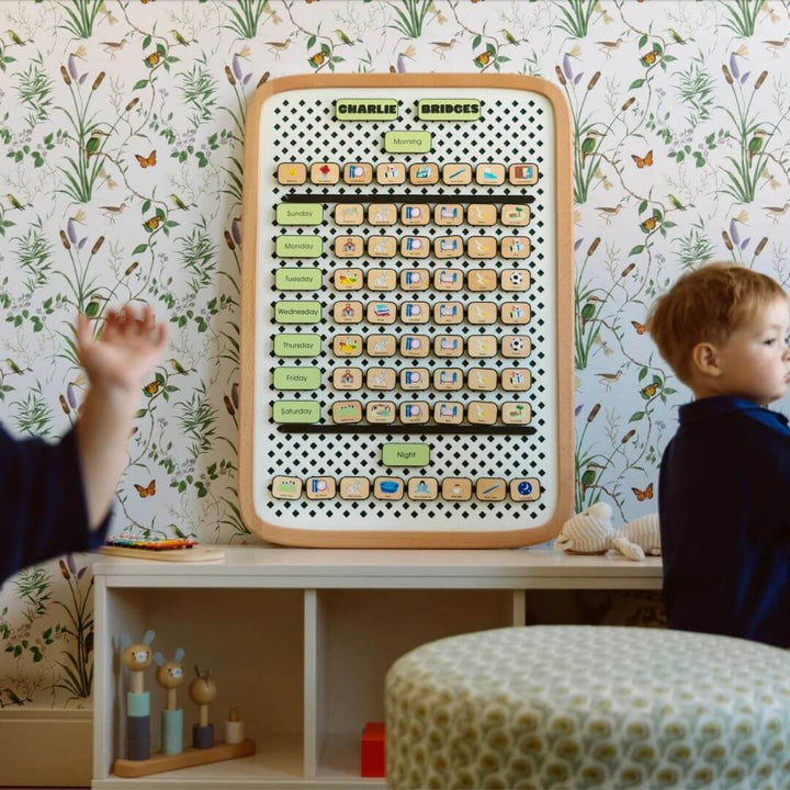 Child interacting with a educational board in a room with floral wallpaper