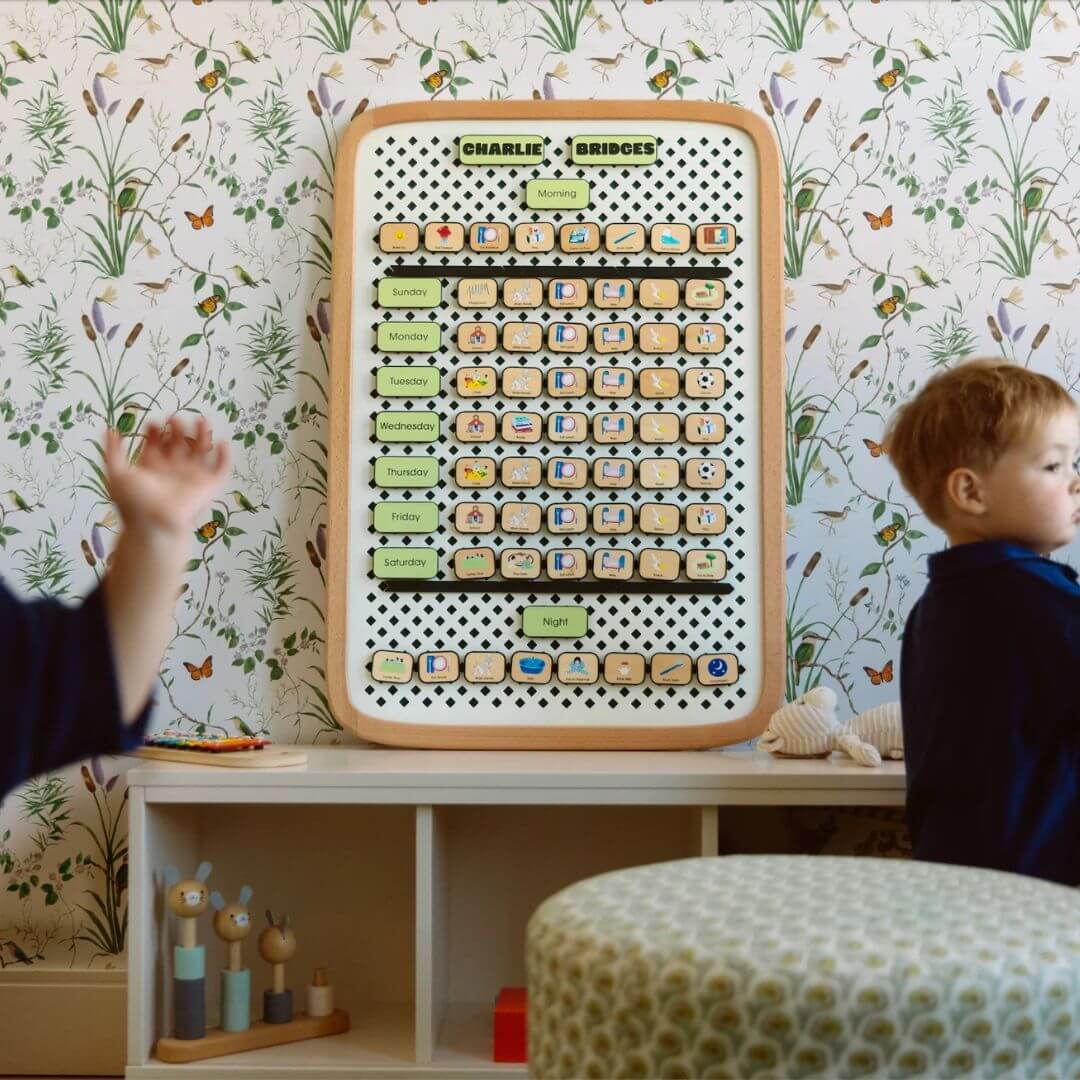 Child interacting with a educational board in a room with floral wallpaper
