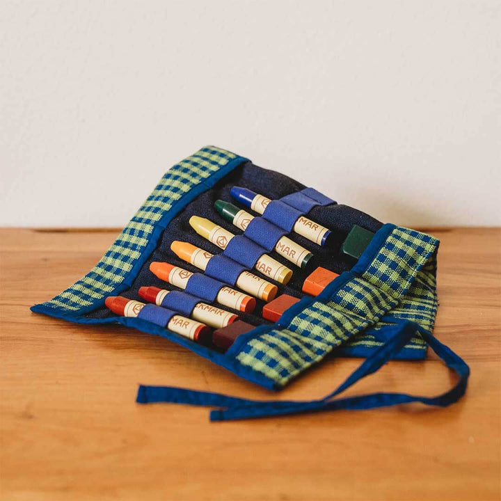 Set of colorful crayons in a green and blue checkered case on a wooden surface