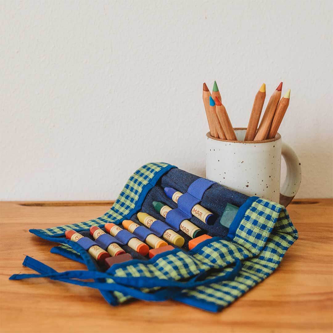 Colorful crayons in a woven holder and wooden mug on a wooden surface.