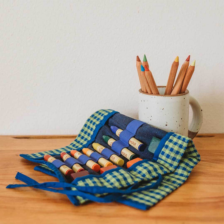 Colorful crayons in a woven holder and wooden mug on a wooden surface.