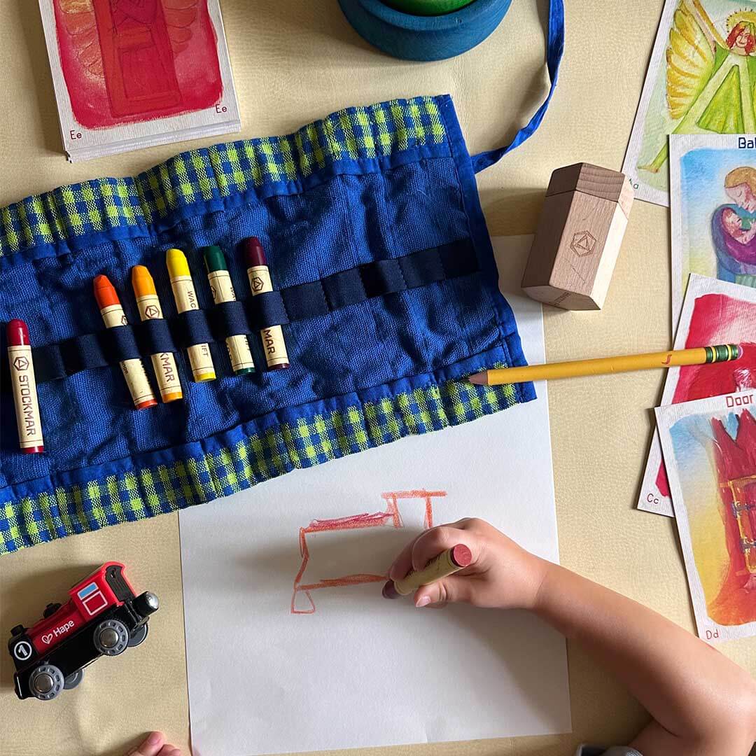 Child drawing with crayons on a piece of paper, surrounded by art supplies.