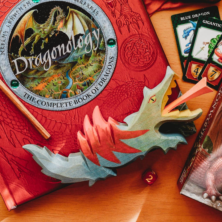 A wooden dragon on a red Dragonology book on a wooden table.