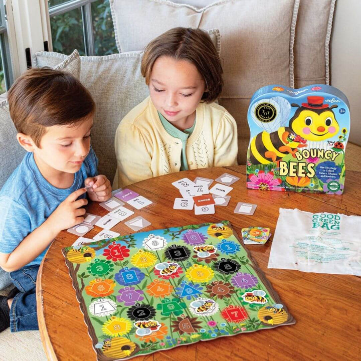 Two children playing with a board game titled 'Bouncy Bees' on a wooden table.