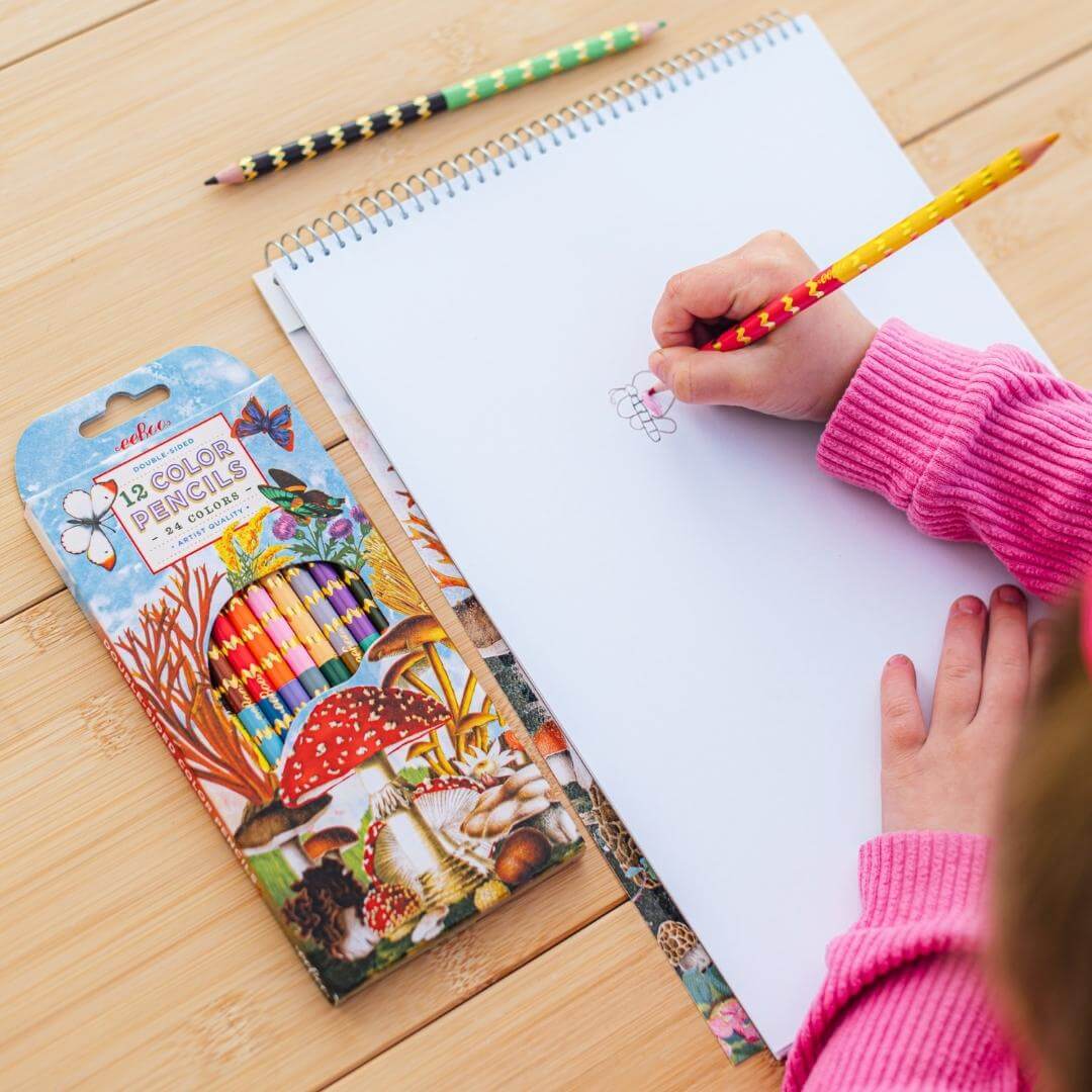 Child coloring with eeBoo mushroom themed colored pencils on a matching sketchbook.