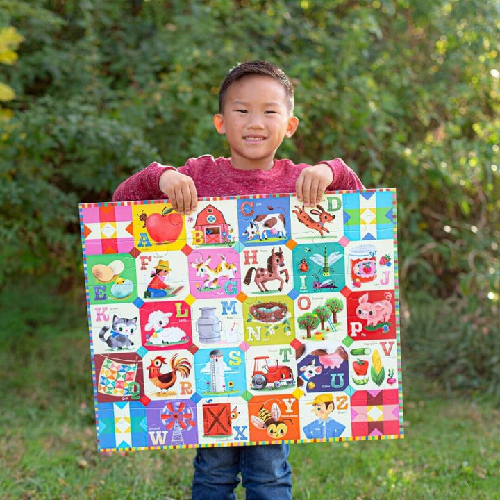 A child holds up the completed eeBoo My Farm Alphabet 36 pc puzzle.
