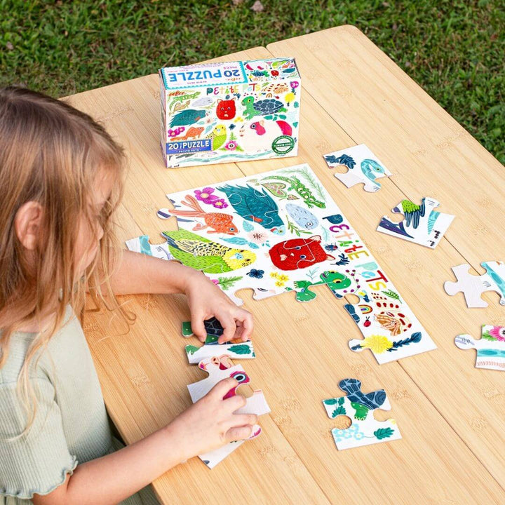 A child sitting at a wooden table doing the 20 pc Petite Pets puzzle from eeBoo.