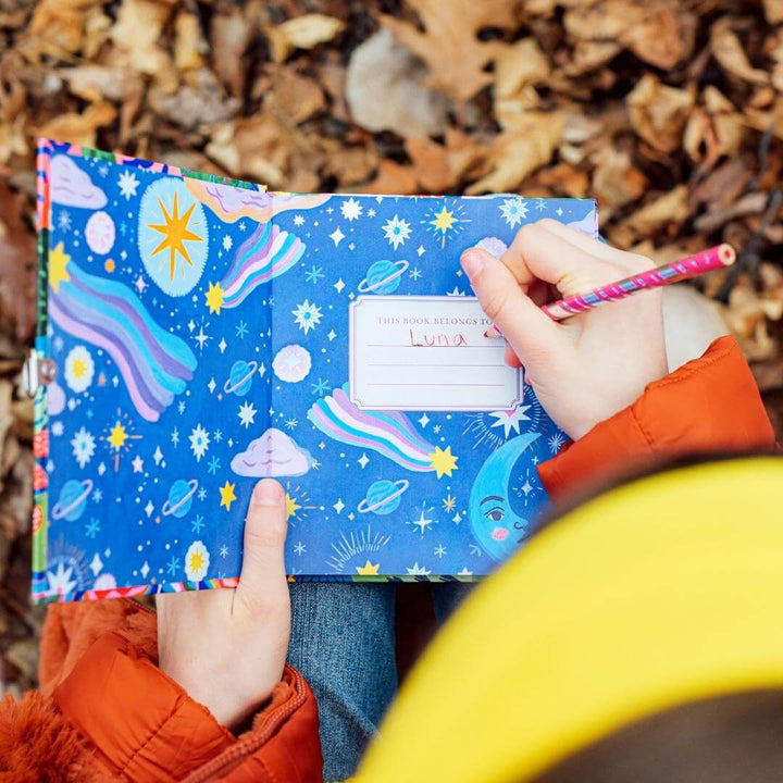 Child writing their name, Luna, in the eeBoo Fawn & Sun Journal with fall leaves in the background.