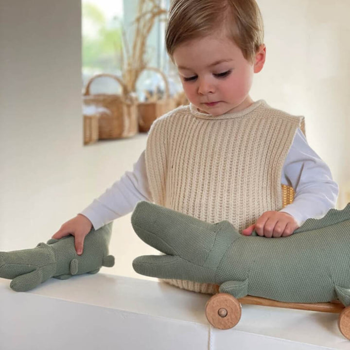 Child playing with a green toy alligator on a white surface