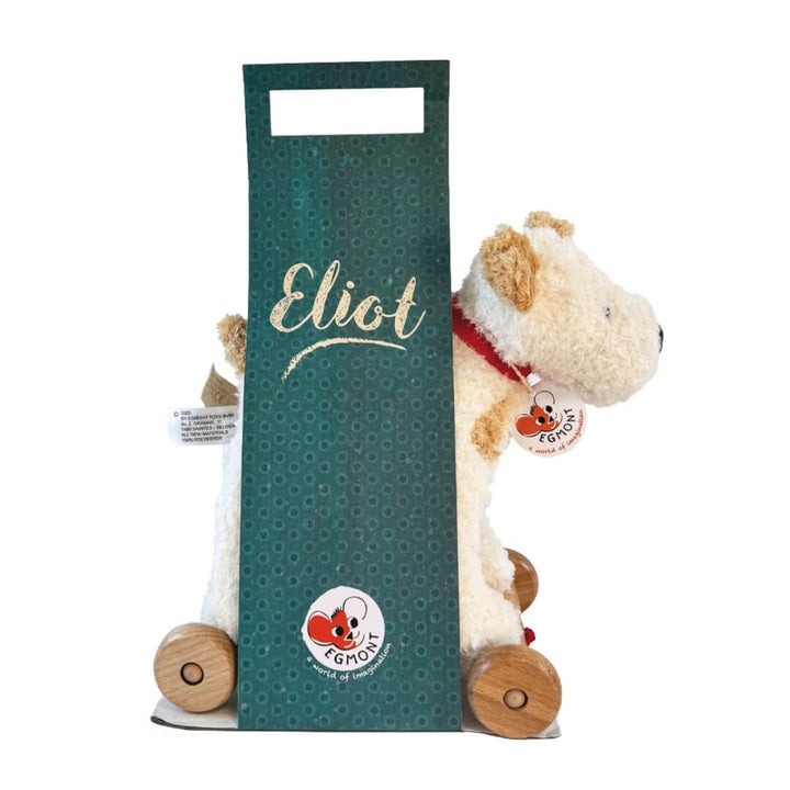Soft plush Eliot Dog pull-along toy with a red cord and sturdy wooden wheels, designed for toddlers to push or pull during active play shown  in it's cardboard package against a white background.