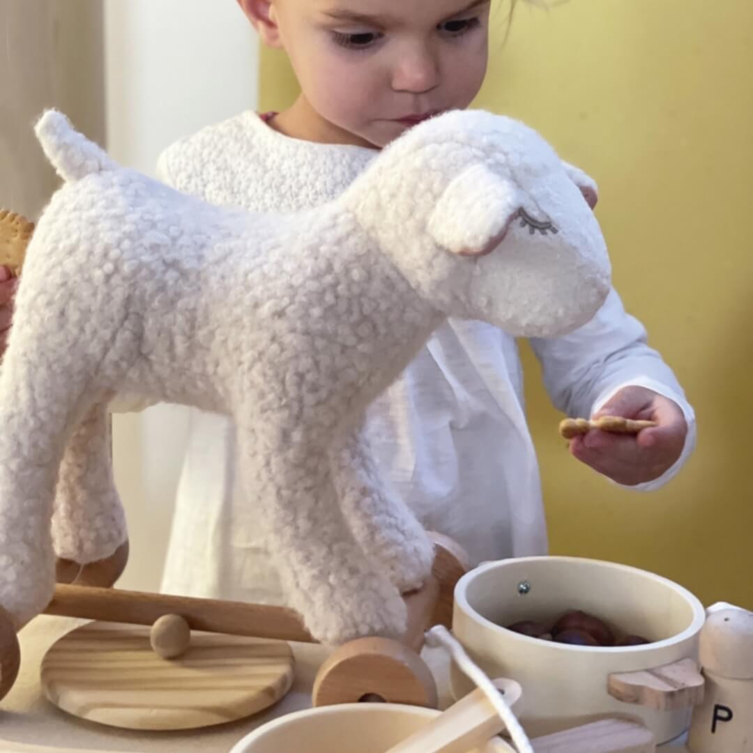 Child playing with a pull-along toy sheep and wooden kitchen set