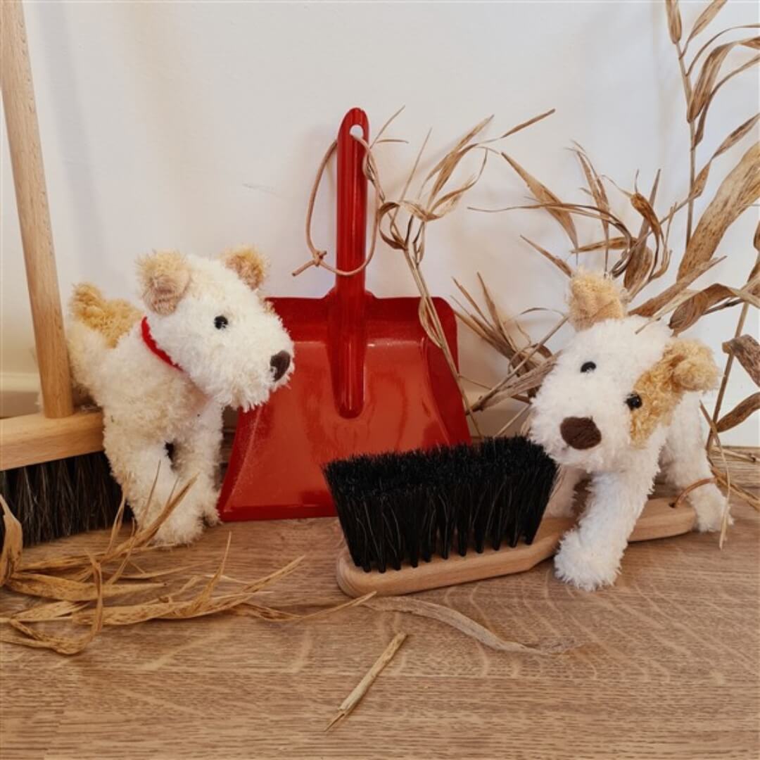 A red metal dustpan and brush set pictured with two stuffed puppy dogs.