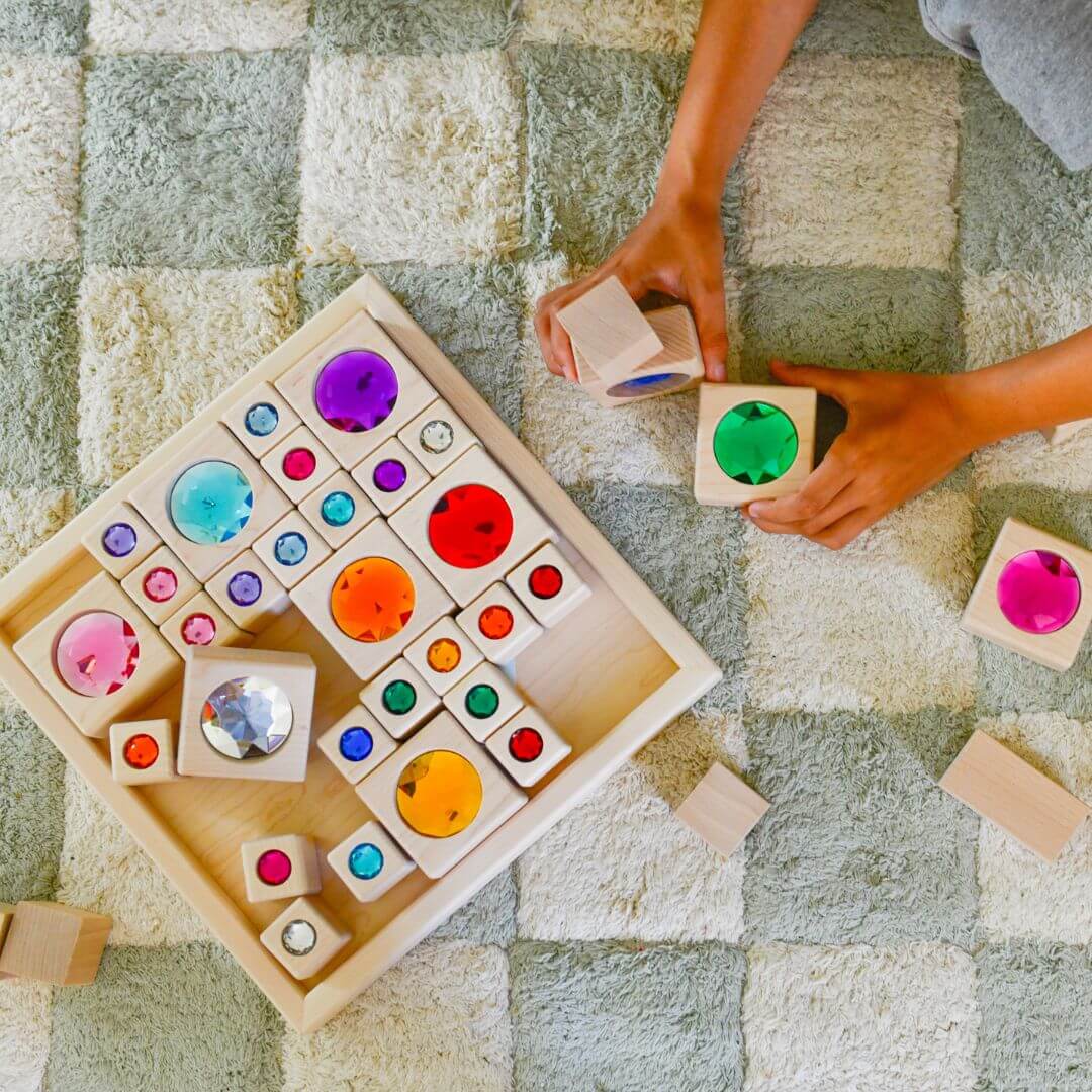 Colorful wooden blocks with embedded round gems on a checkered rug.