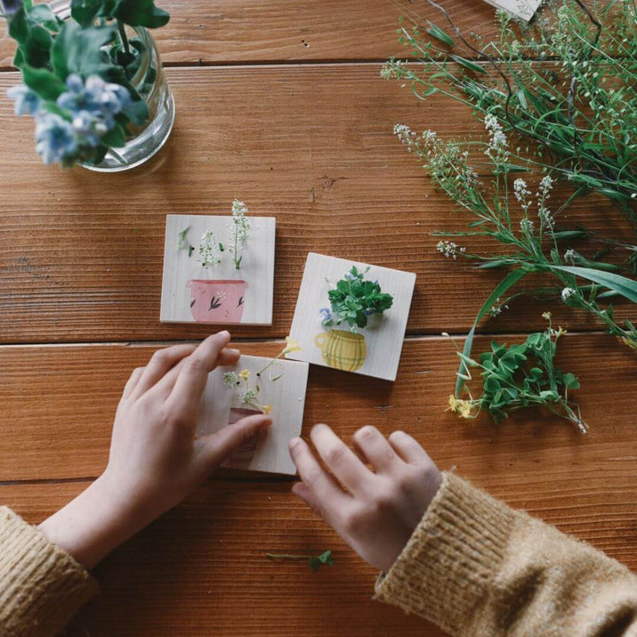 Child’s hands opening Grapat Advent Calendar boxes with illustrated lids, surrounded by flowers on a wooden table – Bella Luna Toys.