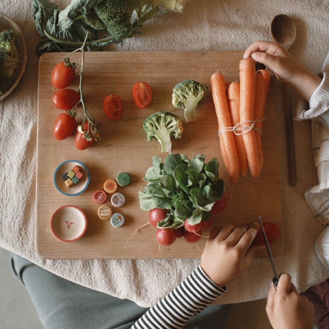 Children arranging fresh vegetables alongside small wooden treasures from the Grapat 2025 Advent Calendar on a wooden cutting board – Bella Luna Toys.