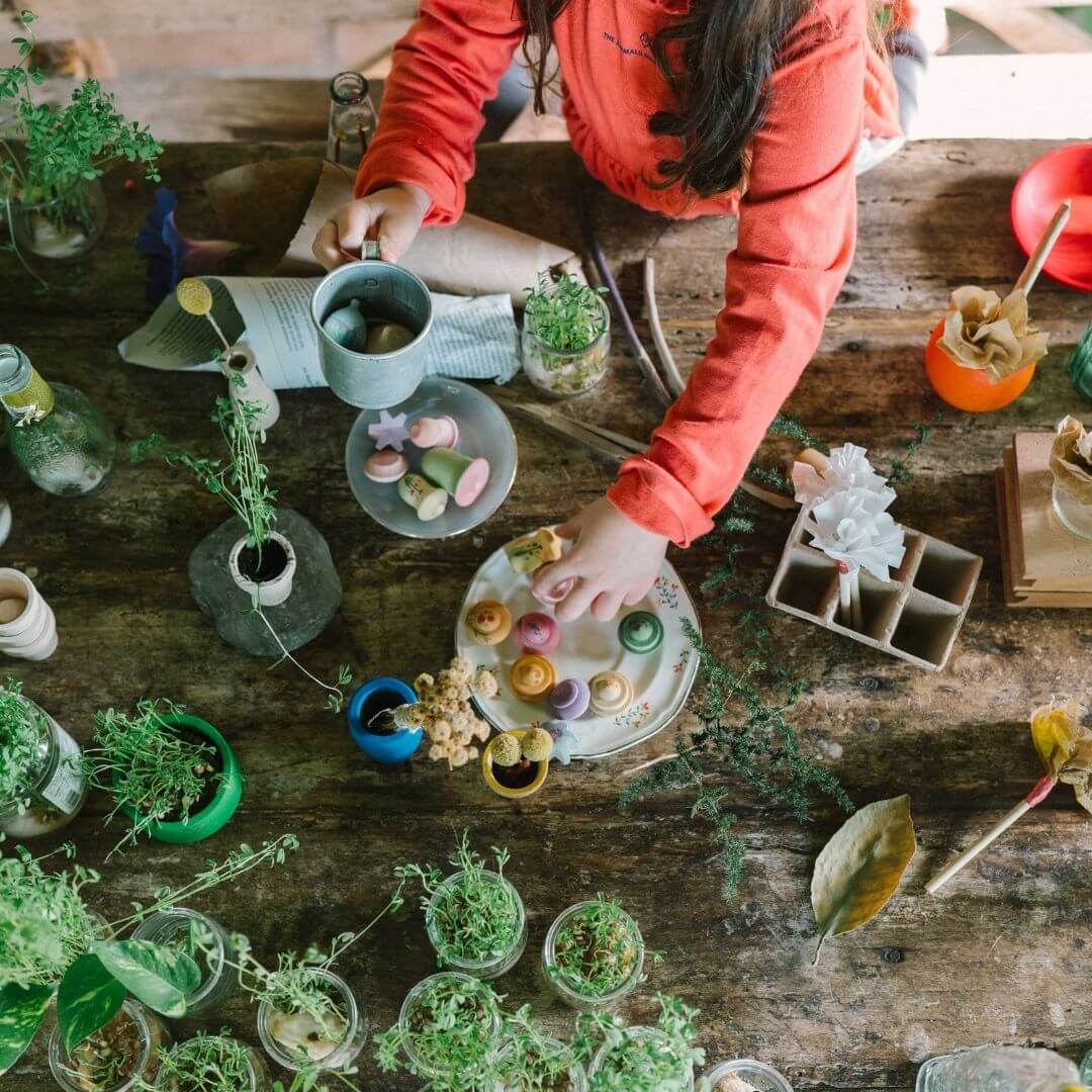 Grapat -A child playing outside with the Grapat Flower Meadow set with 18 hand-painted wooden flower pieces in soft pastel colors, shown with lots of plants - Bella Luna Toys