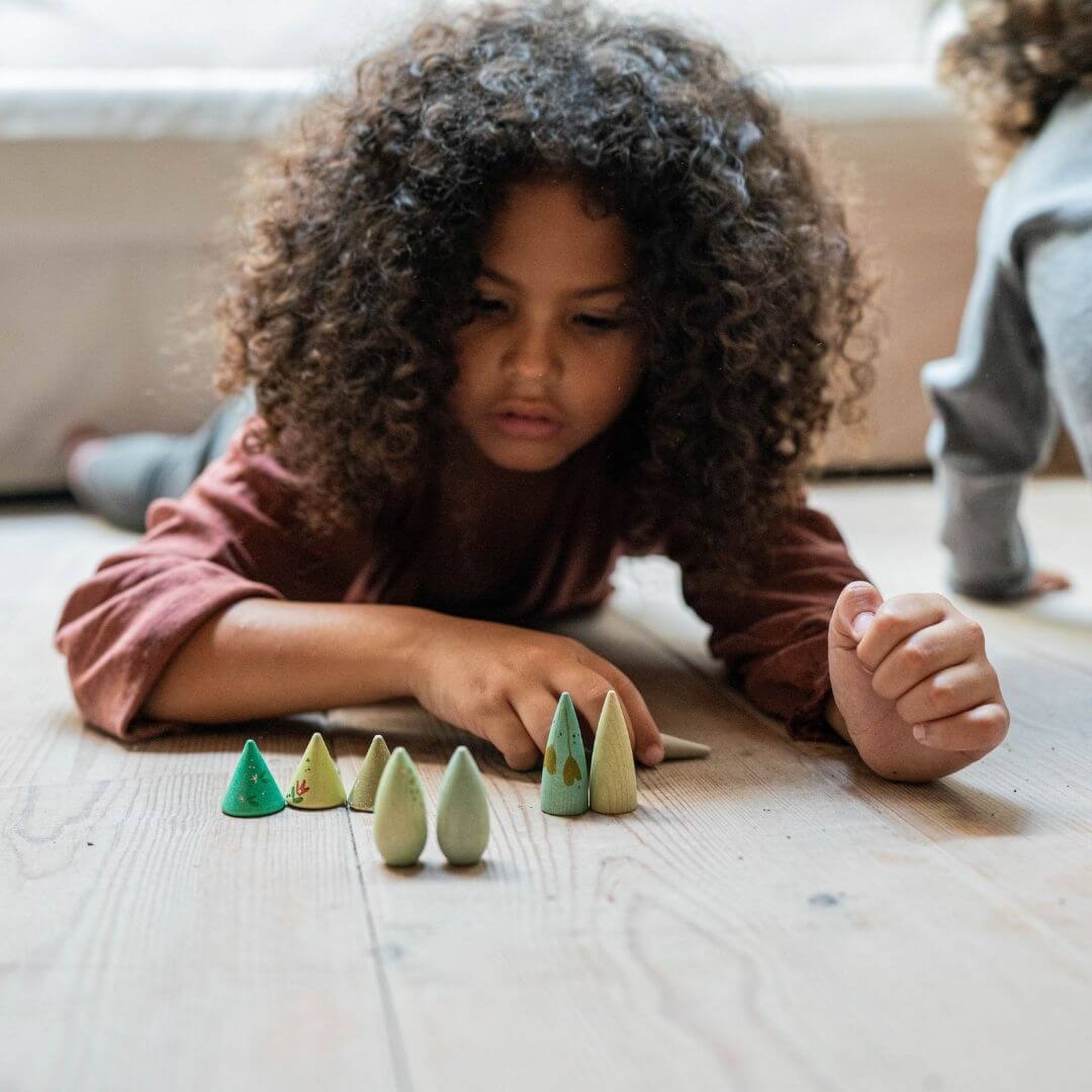 Child playing on the floor with Grapat Forest Trees wooden toy set for small world play, featuring 18 nature-inspired tree pieces - Bella Luna Toys